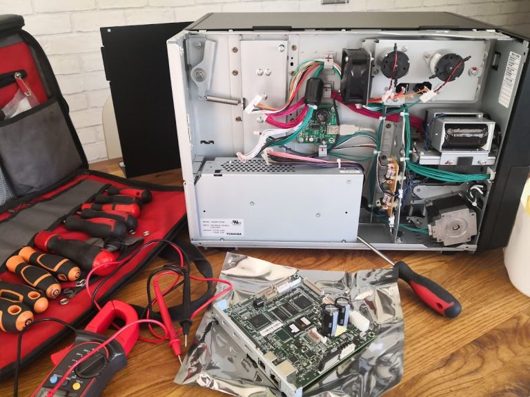Thermal printer opened up for repair on a workbench with engineer's tools